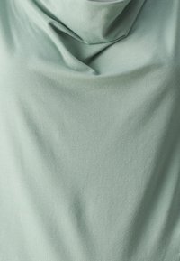 Světlá zelená, měkká tkanina s drapovaným, texturovaným povrchem. Materiál vypadá hladce a mírně elasticky, s jemnými záhyby po celém povrchu.
