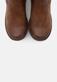 Bottes à cheville en cuir marron avec une texture lisse, des bouts arrondis et des coutures contrastées le long de la semelle. Design minimaliste et matériau durable.