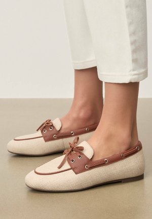 Beżowe tekstylne mokasyny z brązowymi skórzanymi akcentami, okrągłym noskiem i ozdobnymi sznurowadłami. Płaska podeszwa z metalowymi oczkami.