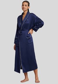 Ρόμπα από σατέν σε ναυτικό μπλε με λευκή διακόσμηση, μακριά μανίκια και ζώνη στη μέση. Διαθέτει τσέπες και σχεδιασμό μήκους μέχρι τη μέση της γάμπας για καθημερινή χρήση.