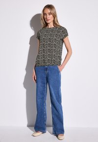 Schwarz-weißer gemusterter Kurzarm-Top, kombiniert mit blauen weiten Jeans und hellen flachen Schuhen. Glatter, weicher Stoff mit lockerer Passform.