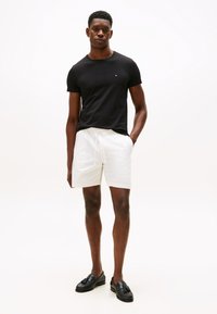 Črna kratka majica s kratkimi rokavi in majhnim logotipom, kombinirana z belimi bombažnimi hlačkami in črnimi loaferji z resicami.