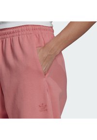 Růžové tepláky s žebrovaným pasem, bočními kapsami a vyšitým logem na dolním lemu, vyrobené z měkké, prodyšné látky.