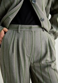 Skräddarsydd kostym i grått med näverstickad mönster och gröna ränder; har en skräddarsydd passform, byxor med veck fram och en kavaj med två knappar.