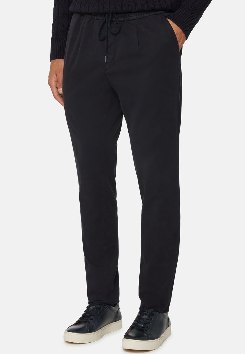 Mustat housut, joissa on joustava vyötärö ja kiristysnauha, yhdistettynä tummiin tennareihin, mallitut neulepuseron kanssa.