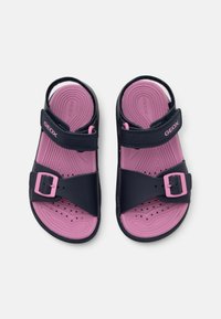 Zwei Sandalen mit einem dunkelblauen Obermaterial und einer pinken Sohle. Das Design umfasst eine Schnalle und ein strukturiertes Fußbett mit Perforationen für Atmungsaktivität.
