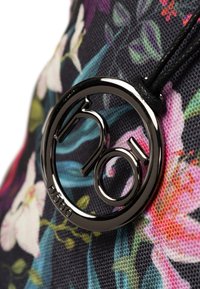 Bloemachtig stoffen tas met een zwart, glanzend metalen logo accent. Het materiaal heeft een textuur met levendige kleuren, waaronder paars, roze en groen.