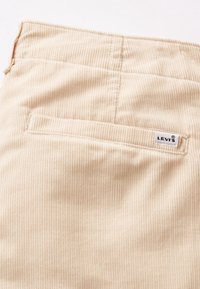 Tissu en velours côtelé beige avec une poche arrière horizontale et une petite étiquette blanche Levi's cousue près du bord de la poche.