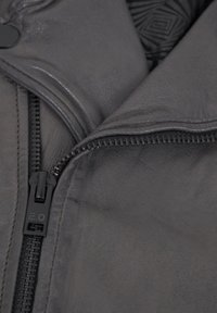 Schwarze Lederjacke mit glatter Textur, einem auffälligen Reißverschluss und einem gemusterten Innenfutter, das funktionale Designdetails betont.