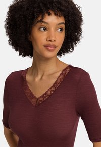 Bordowy top o ryflowanej fakturze i krótkich rękawach, z koronkowym wykończeniem wzdłuż dekoltu w kształcie litery V.