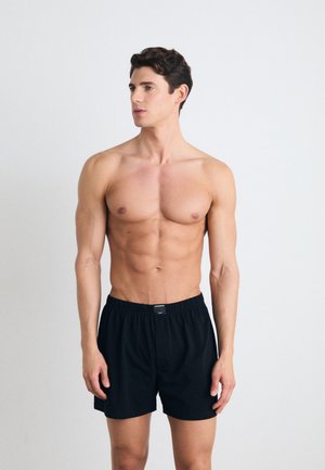 Shorts noirs avec ceinture élastique, à coupe relaxée. Tissu lisse, longueur genoux, design minimal, sans motifs ni accents visibles.