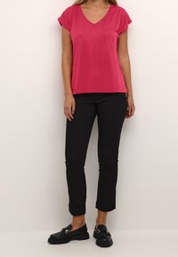 Top rosa de cuello en V con mangas cortas, combinado con pantalones ajustados negros y mocasines negros. La tela parece suave con un diseño casual.
