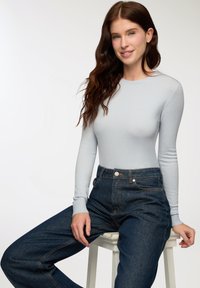 Maglietta azzurra chiara a maniche lunghe realizzata in un tessuto morbido, abbinata a jeans scuri a vita alta con cuciture evidenti e tasche anteriori.