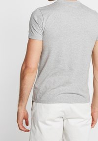 Graues, eng anliegendes T-Shirt mit kurzen Ärmeln, aus glattem Baumwollstoff gefertigt. Verfügt über einen runden Ausschnitt und einen schlichten Rücken. Akzente setzen minimale Nähte.
