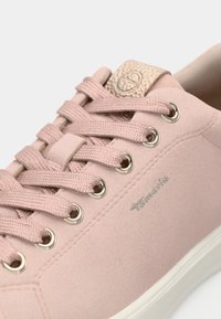 Gros plan sur une chaussure de sport rose à lacets avec des œillets métalliques et une languette texturée, présentant une marque sur le côté et une semelle douce.
