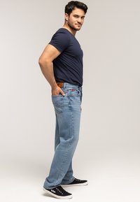 Jasnoniebieskie jeansy z denimu o prostym kroju, z przeszyciami, bocznymi kieszeniami i brązową skórzaną naszywką na pasku w talii.