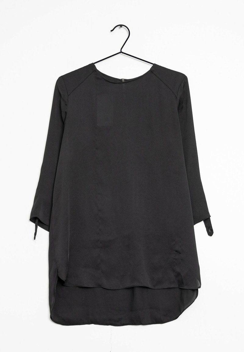 Tunique noire à manches longues avec un col rond, texture lisse et un ourlet arrière plus long. Présente des manches retroussées avec des détails de nouage.