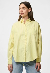 Camicia a righe gialle con collare button-down, maniche lunghe e taschino frontale. Tessuto morbido con vestibilità rilassata. Abbinata a jeans azzurri chiari.