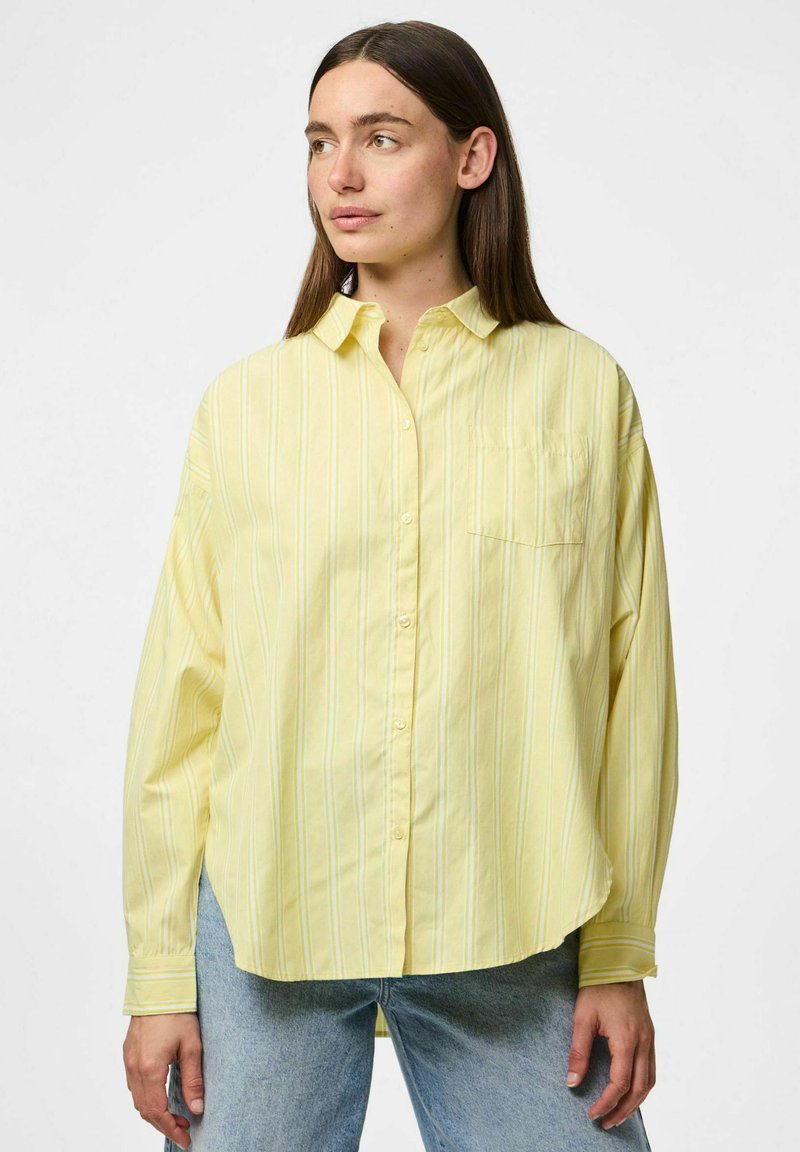 Camicia a righe gialle con collare button-down, maniche lunghe e taschino frontale. Tessuto morbido con vestibilità rilassata. Abbinata a jeans azzurri chiari.