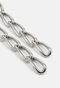 Metal kæde med forstørrede, ovale led og en skinnende sølvfinish. Glat tekstur med synlige forbindelser mellem leddene.