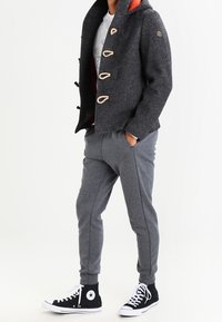 Grå uldne duffelcoat med orange foer, toggles, grå sweatpants og sorte højtop sneakers. Sættet har et afslappet look.
