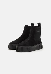 Černé semišové kotníkové boty s silnou texturovanou podrážkou, elastickými bočními panely a poutky pro snadné obouvání. Minimalistický design s elegantním siluetou.