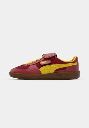 Red and yellow sneaker with a leather and suede upper, featuring a padded tongue, laces, and a textured rubber sole. Gold branding accents.