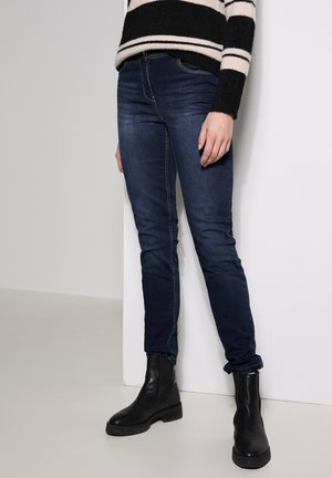Jean skinny en denim bleu foncé avec une légère extensibilité, doté d'une taille standard et de revers, associé à des bottines noires.