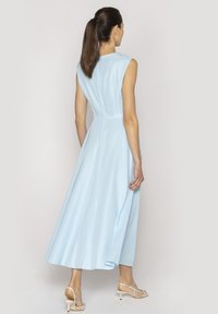 Jasnoniebieska, bezrękawnikowa sukienka midi z dopasowaną górą, zwiewnym dołem i gładką teksturą. Połączona z cielistymi, odkrytymi butami na obcasie.