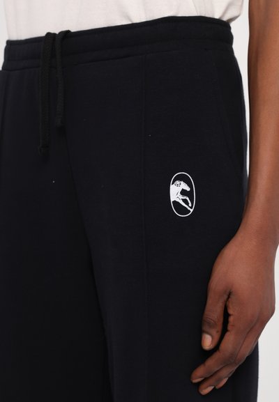 Black sweatpants in soft fabric with an elastic waistband and drawstring. Features a white logo of a leaping dog on the left side.