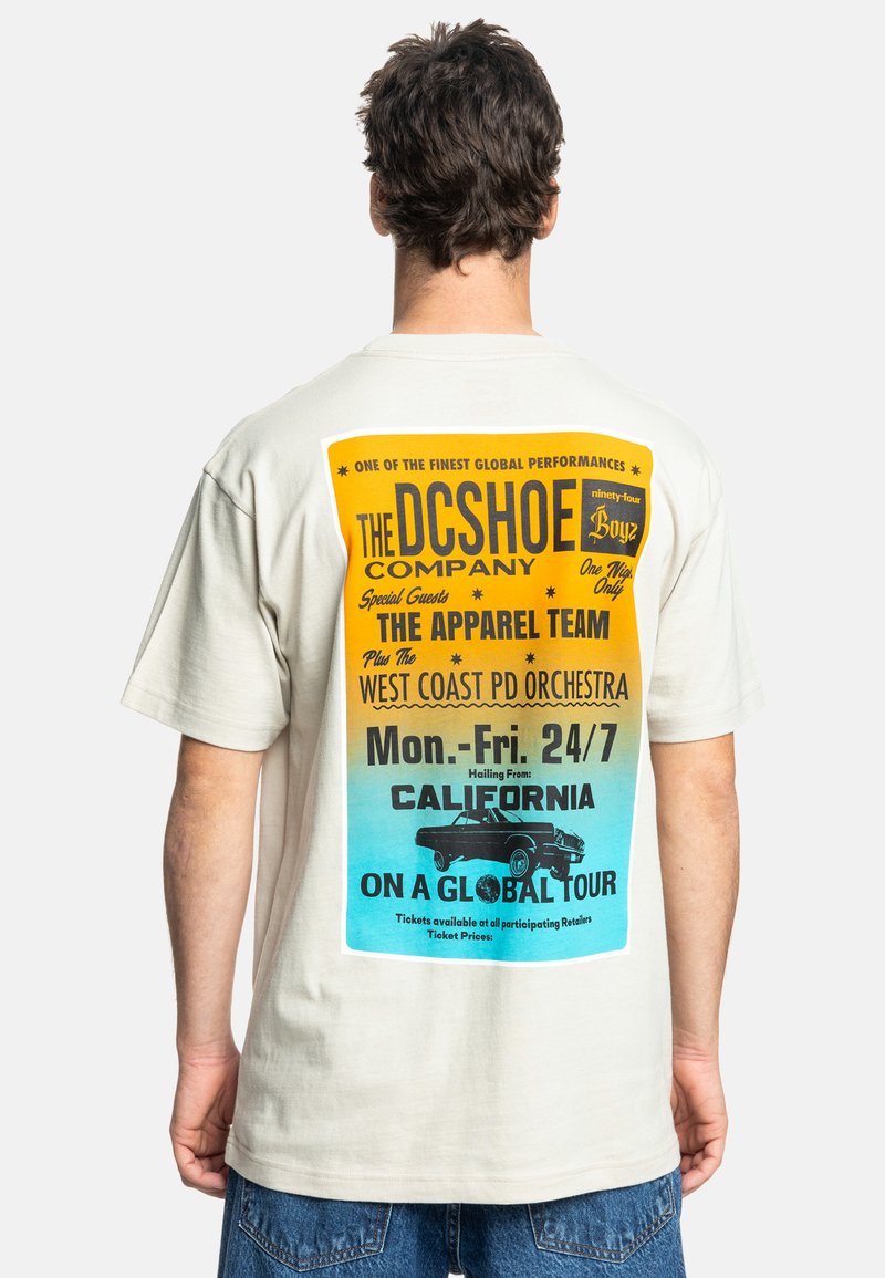 Beige T-Shirt mit kurzen Ärmeln, das auf der Rückseite einen bunten Grafikdruck mit Text und einer Illustration eines Autos in Blau, Gelb und Schwarz zeigt.