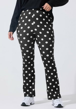 Sorte tætsiddende bukser med store hvide polkaprikker, båret med hvide sneakers og en sort langærmet top, vist fra taljen til fødderne.