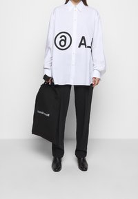 Vit oversized skjorta med djärva svarta grafik, parat med svarta byxor och en svart tygväska med vit text. Slät tygstruktur.