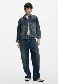 Džínová bunda s ramennými akcentmi a vreckami s klopou, skombinovaná s modrými širokými nohavicami. Obe kusy majú bledý jemný vzhľad a voľný strih.