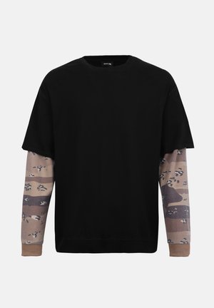 Μαύρο φούτερ με κοντά μανίκια, φορεμένο πάνω από μακριά μανίκια με καφέ και ταμπά καμουφλάζ, με ριμπ μανσέτες και στρογγυλή λαιμόκοψη.