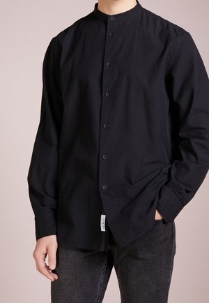 Camicia nera a maniche lunghe con colletto alla coreana, davanti con bottoni e taglio dritto. Realizzata in tessuto leggero con texture minimale.