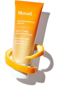 Oranger Tub von Murad Vita-C Triple Exfoliating Facial, mit weißen Akzenten und glatter Oberfläche, umwickelt mit einer getrockneten Orangenschale.