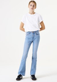 Hellblaue, ausgestellte Jeans mit hoher Taille, Knopfverschluss, Gürtelschlaufen und leichten Used-Effekten. Kombiniert mit einem weißen T-Shirt mit kurzen Ärmeln.