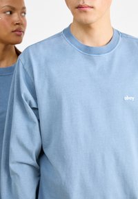 Light blue sweatshirt with long sleeves, crew neck, and a soft texture. Features a small white "obey" logo on the chest.