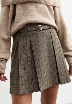 Bruine geruite plooirok met een riem met een rechthoekige gespsluiting en een textuurrijke stof. Gecombineerd met een zacht beige gebreide trui.