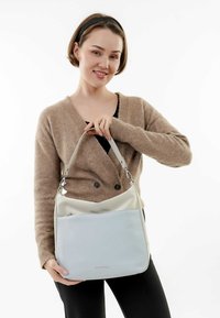 Bolso de mano azul claro y crema con un diseño estructurado, que presenta una correa de hardware plateado, textura suave y un bolsillo externo.