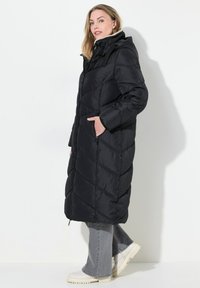 Cappotto lungo nero imbottito con cappuccio, caratterizzato da un motivo a rombi trapuntato, tasche laterali e chiusura con zip. Abbinato a stivali chunky chiari.