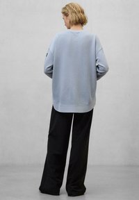 Felpa azzurra con spalle scese e orlo arrotondato, abbinata a pantaloni neri larghi per un look rilassato.