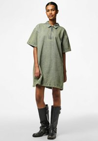 Kratke rukave, zelena traper haljina s ovratnikom i zatvaranjem na pola munje, s bočnim prorezom i ležernim krojem. Uparena s crnim čizmama do koljena.