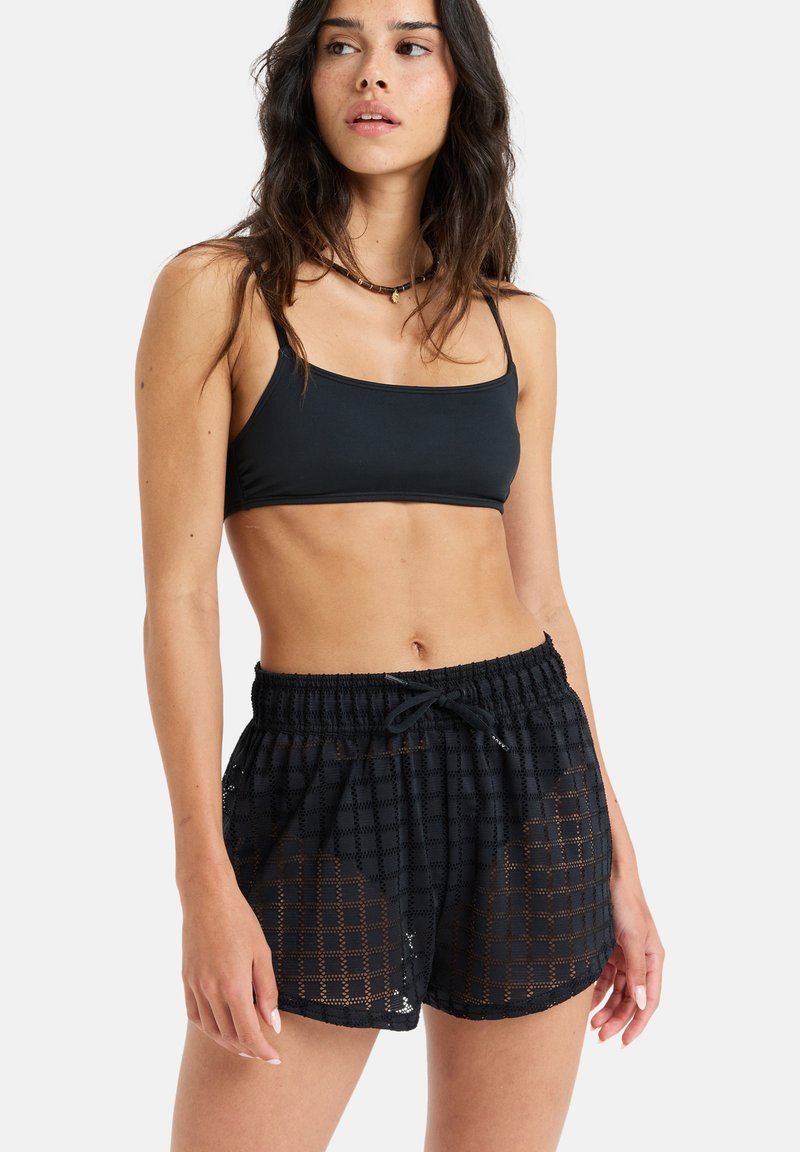 Black mesh shorts with an elastic waistband and drawstring, featuring a square pattern and a relaxed fit. Paired with a matching black crop top.