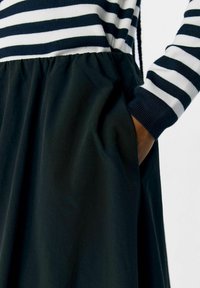 Robe noire avec un haut ajusté comportant des rayures horizontales bleu marine et blanches. Jupe fluide et froncée avec poches et poignets en tricot côtelé.