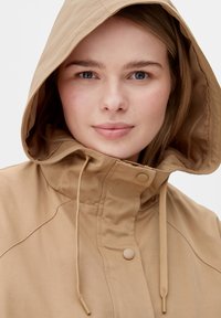 Beige Kapuzenjacke mit lockerer Passform, Knopfverschluss, Zugband am Hals und glattem, einfarbigem Stoff. Sie zeichnet sich durch ein einfaches, funktionales Design aus.