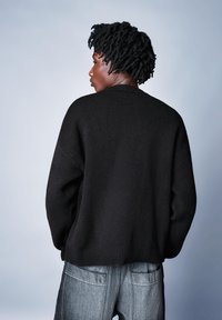 Czarny, oversize'owy sweter z prążkowanym dołem, o dzianinowej fakturze i opuszczonych ramionach, zestawiony z jasnymi dżinsami z denimu.