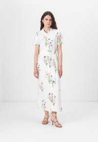 White floral dress with short sleeves, features multicolored flower patterns, a belted waist, and a midi length. Paired with strappy sandals.