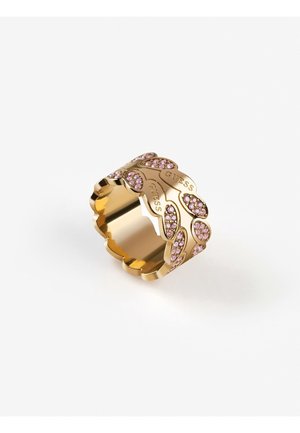 Złoty pierścionek z falistymi krawędziami, ozdobiony różowymi kamieniami szlachetnymi i wygrawerowaną nazwą marki Guess wokół powierzchni.